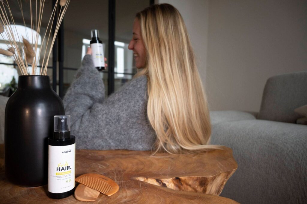 Jeune femme au long cheveux qui tient le produit Feeds Hair avec le sourire